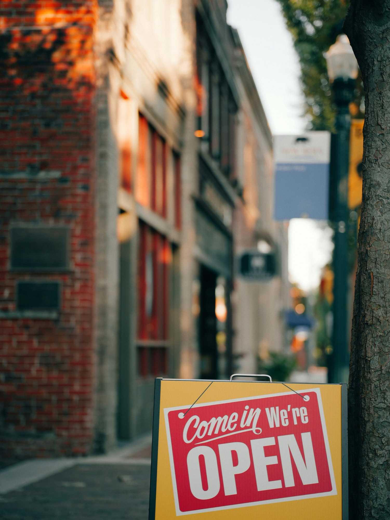 An A-frame sidewalk sign reading &ldquo;Come in, we&rsquo;re open&rdquo; outside a small business